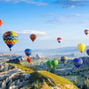 A vibrant landscape featuring rolling hills, valleys, and distant mountains under a blue sky with numerous colorful hot air b
