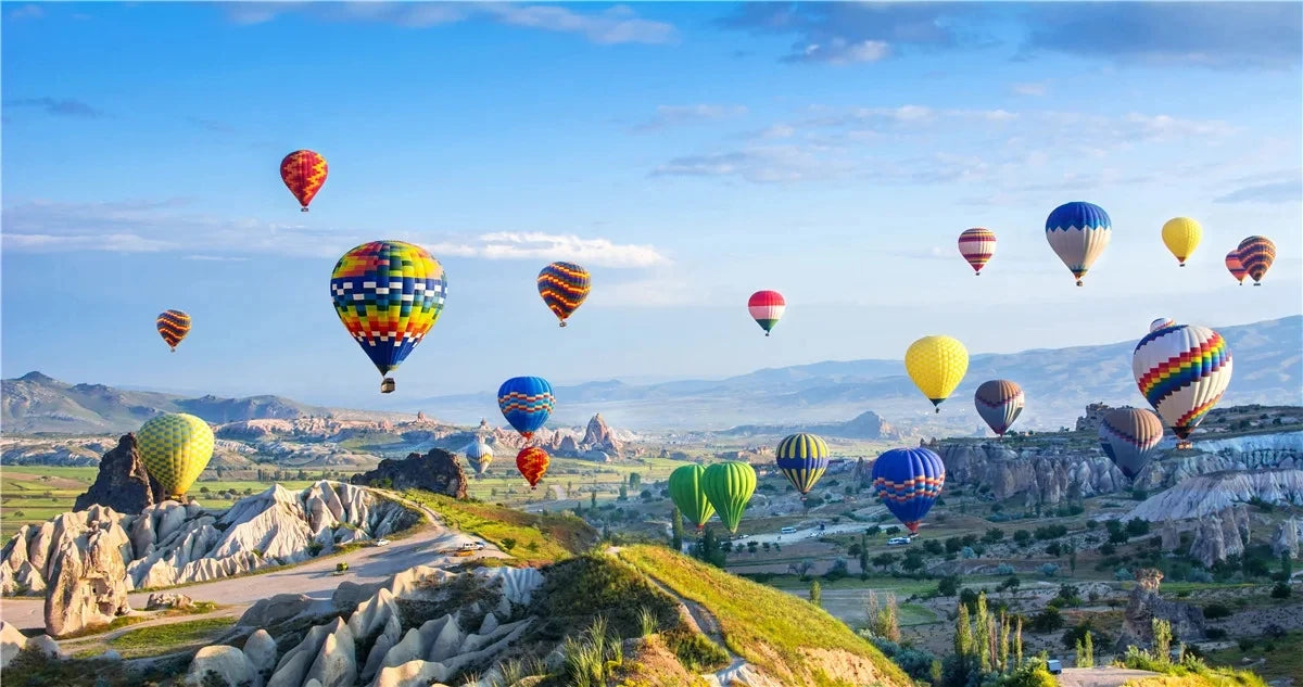 A vibrant landscape featuring rolling hills, valleys, and distant mountains under a blue sky with numerous colorful hot air b