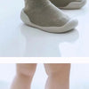 A pair of soft-soled baby first walker socks shoes in beige and orange are shown on a white surface.