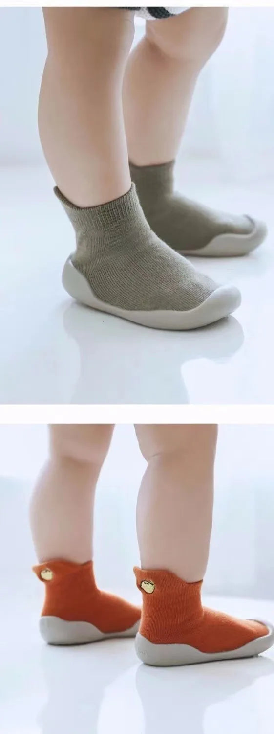 A pair of soft-soled baby first walker socks shoes in beige and orange are shown on a white surface.