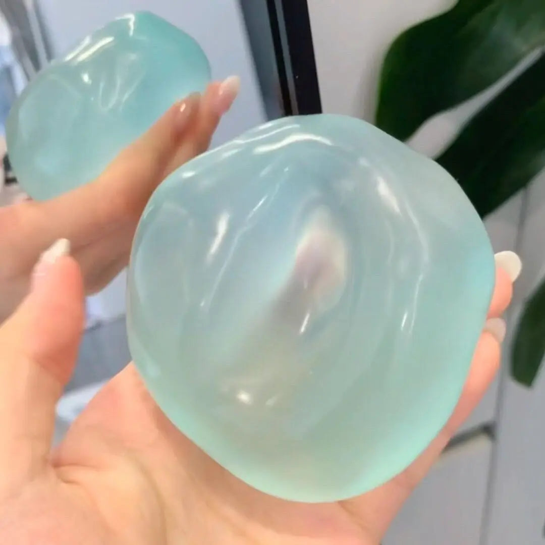 A hand holds a translucent, pale blue silicone squeeze ball used for stress relief.