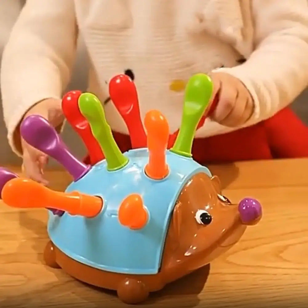 A child is holding a plastic hedgehog toy with colorful protrusions for fine motor skill practice.