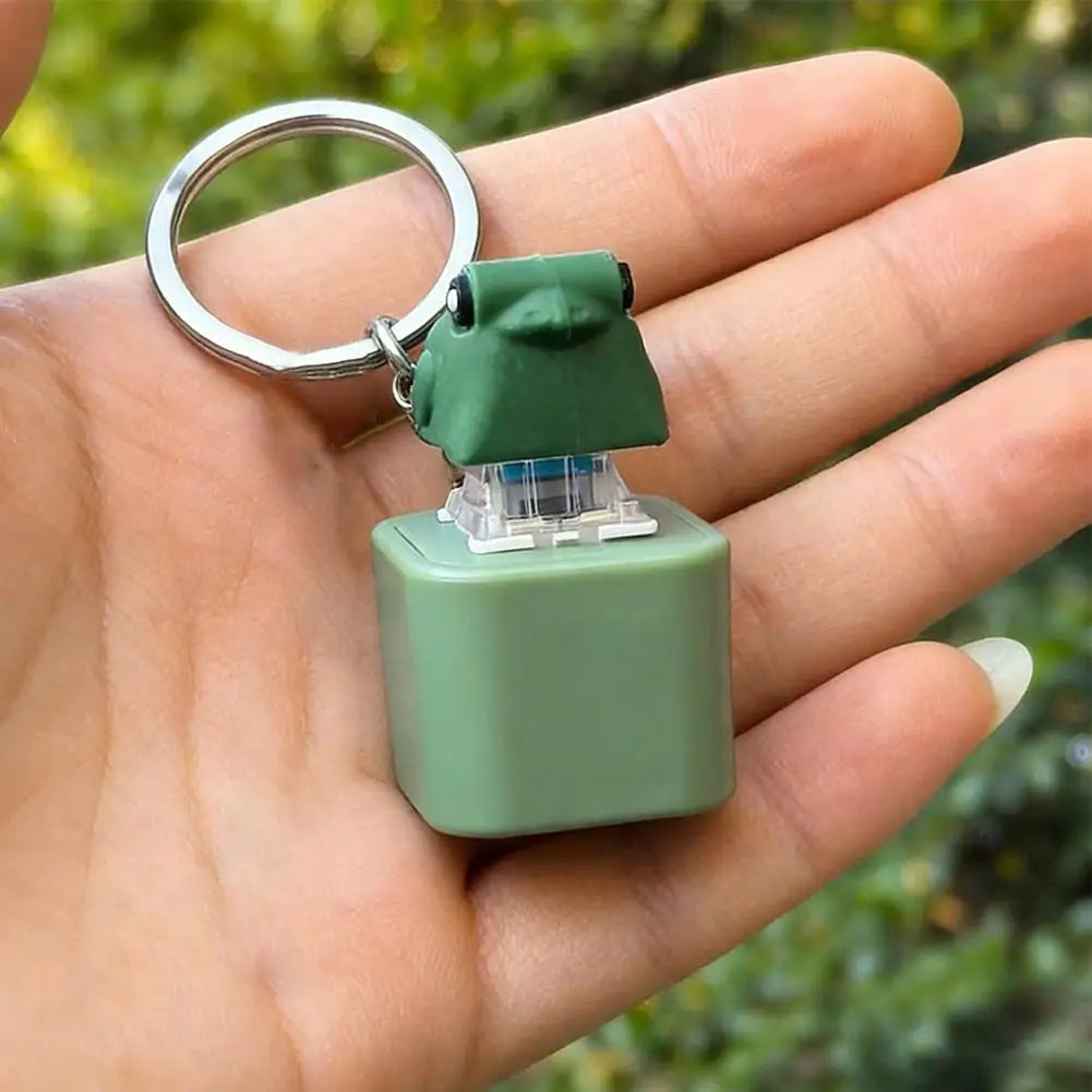 Grüne, froschförmige Fidget-Schlüsselanhänger mit Metallring, in der Hand eines Menschen gehalten.
