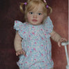 A realistic reborn baby doll kit named Pippa with blonde hair and pink hair accessories wearing a floral dress.