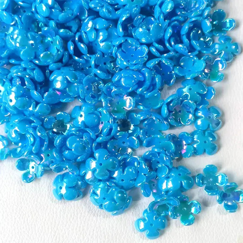 A pile of bright blue acrylic beads shaped like four-petal flowers for jewelry making