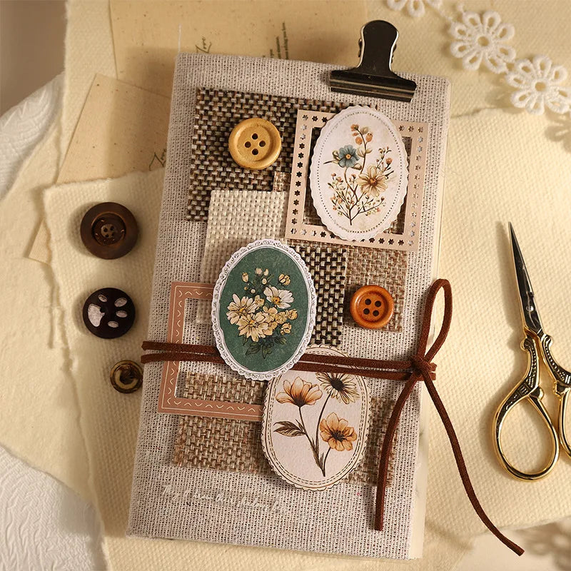 A collection of vintage floral stickers, including pressed flowers and small buttons, arranged on a beige fabric background.
