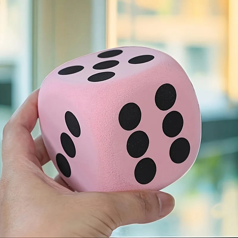 A hand holds a pink jumbo soft foam die with black dots, showing its texture and size.