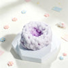 A light purple squishy sensory stress ball with a bubbly texture resting on a white block, surrounded by small pastel confett