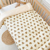 A beige fleece blanket with a small brown animal pattern is draped over a wooden crib railing.