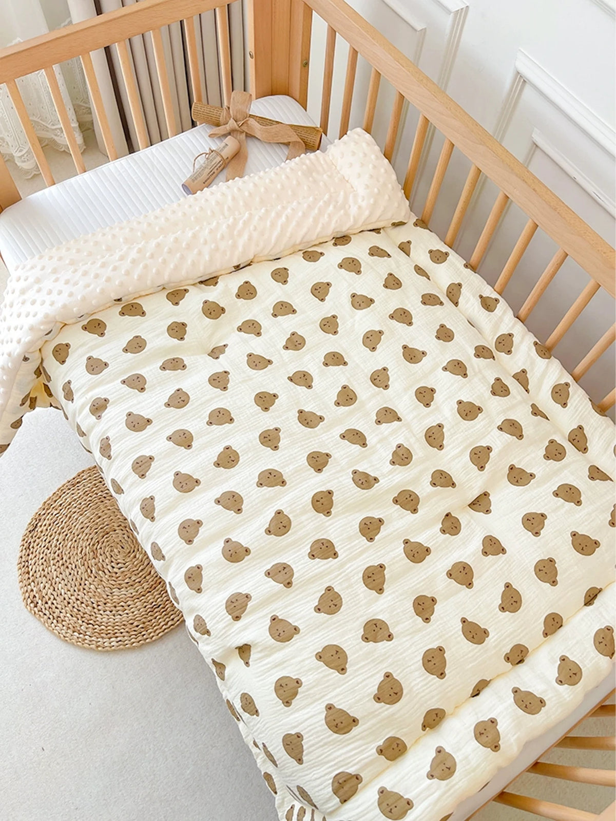 A beige fleece blanket with a small brown animal pattern is draped over a wooden crib railing.