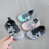 A hand holds a pair of breathable mesh toddler walking shoes in gray and pink tones.