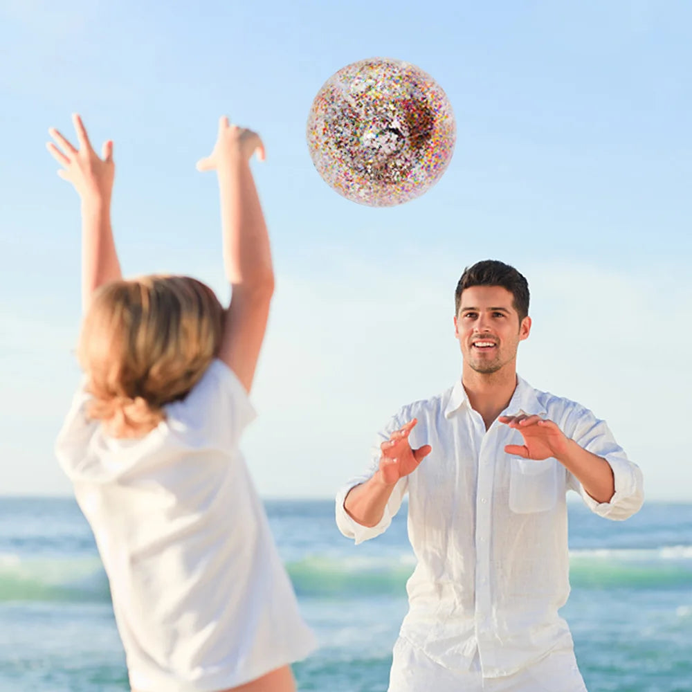 A man and a woman are playing with a colorful sequined inflatable beach ball near the ocean.