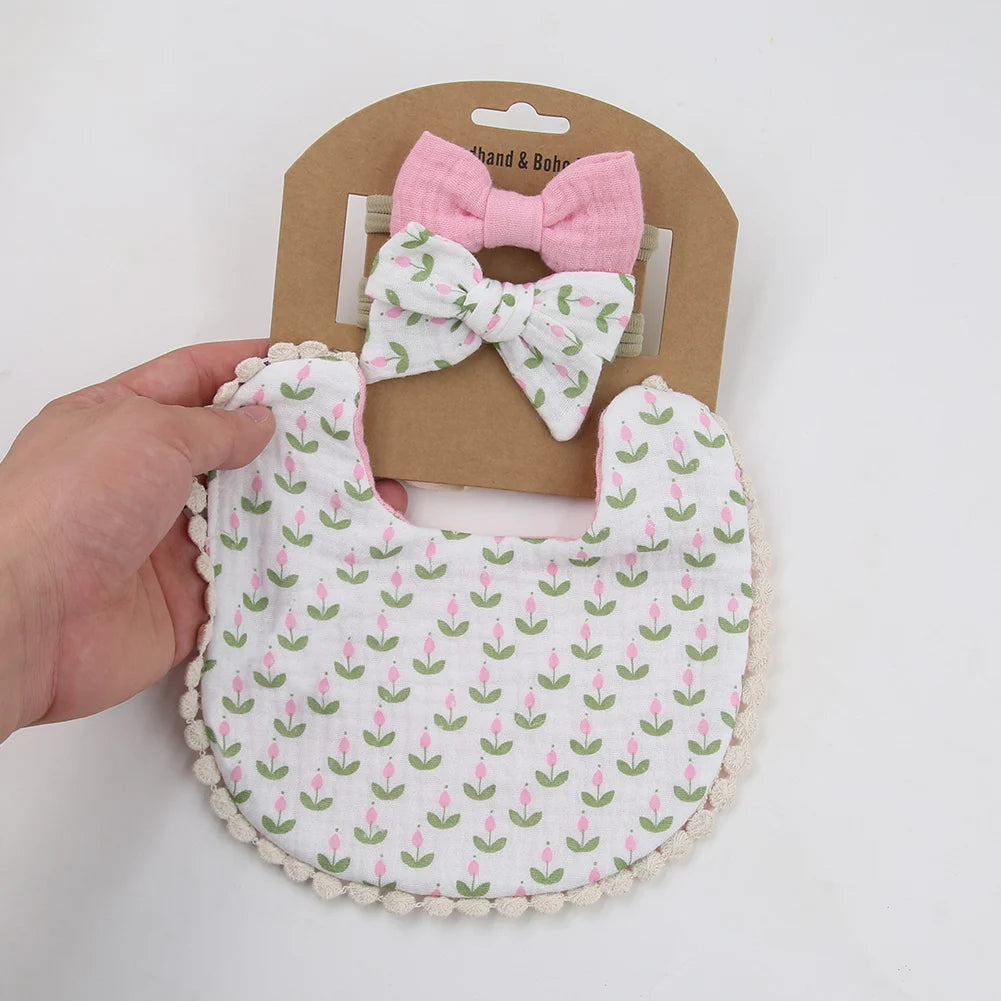 A set of three pink and white floral baby flower bibs and a matching bow headband displayed on brown cardstock.