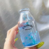 A hand holds a clear glass bottle filled with blue liquid and sparkling stars, used as a sensory toy.