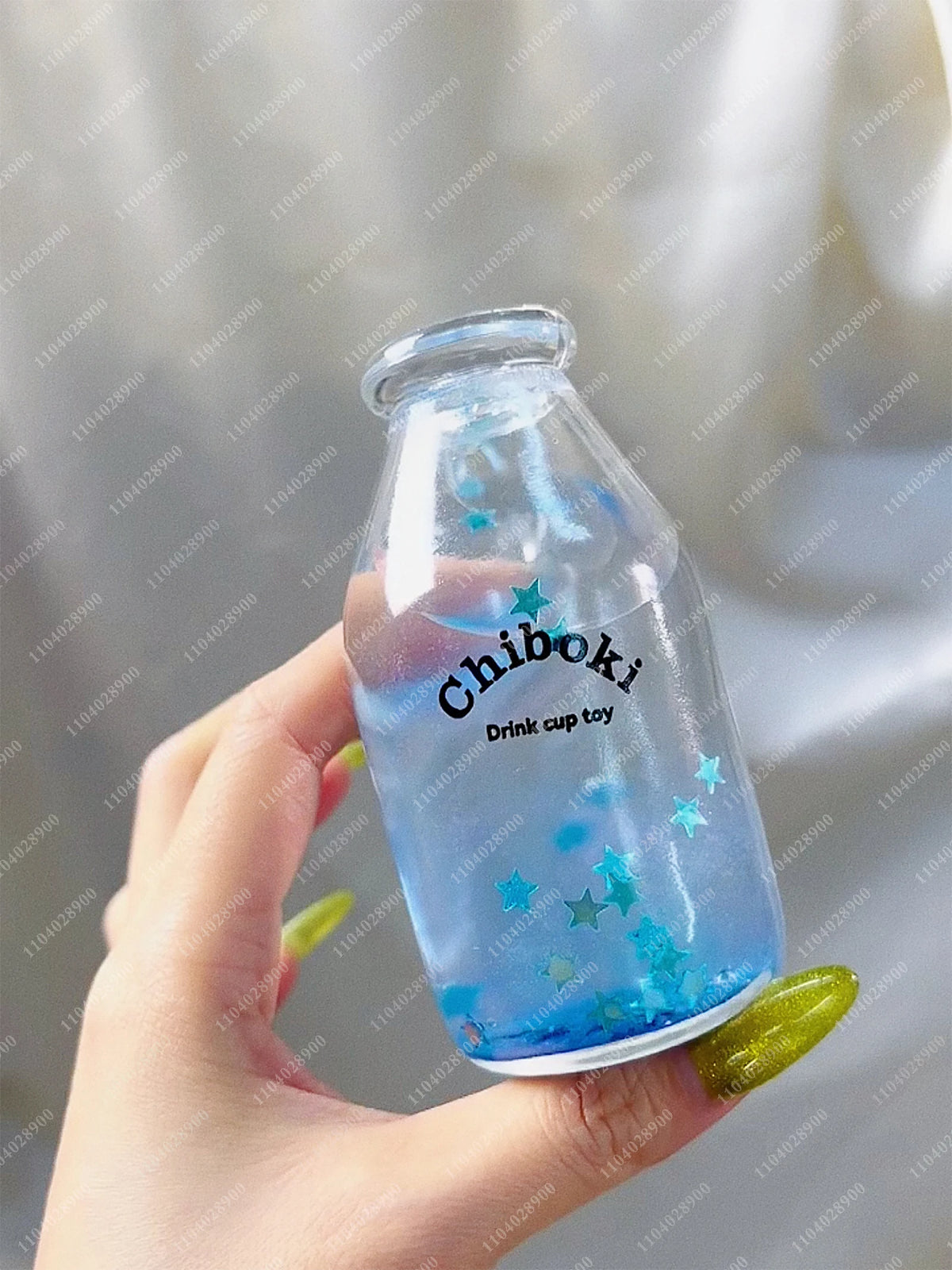 A hand holds a clear glass bottle filled with blue liquid and sparkling stars, used as a sensory toy.