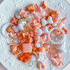 A collection of colorful acrylic bow and flower beads in pink, orange, and white are displayed on a white plate.