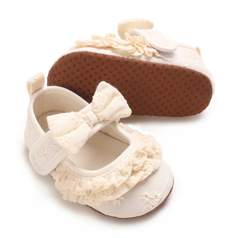 A pair of cream-colored baby walking shoes with anti-slip brown soles and decorative fringe.