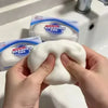 A hand holds a white squishy stress ball fidget toy next to its packaging in a bathroom sink.
