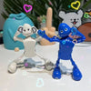A white wind-up dancing robot toy and a blue wind-up dancing robot toy are displayed on a white surface.