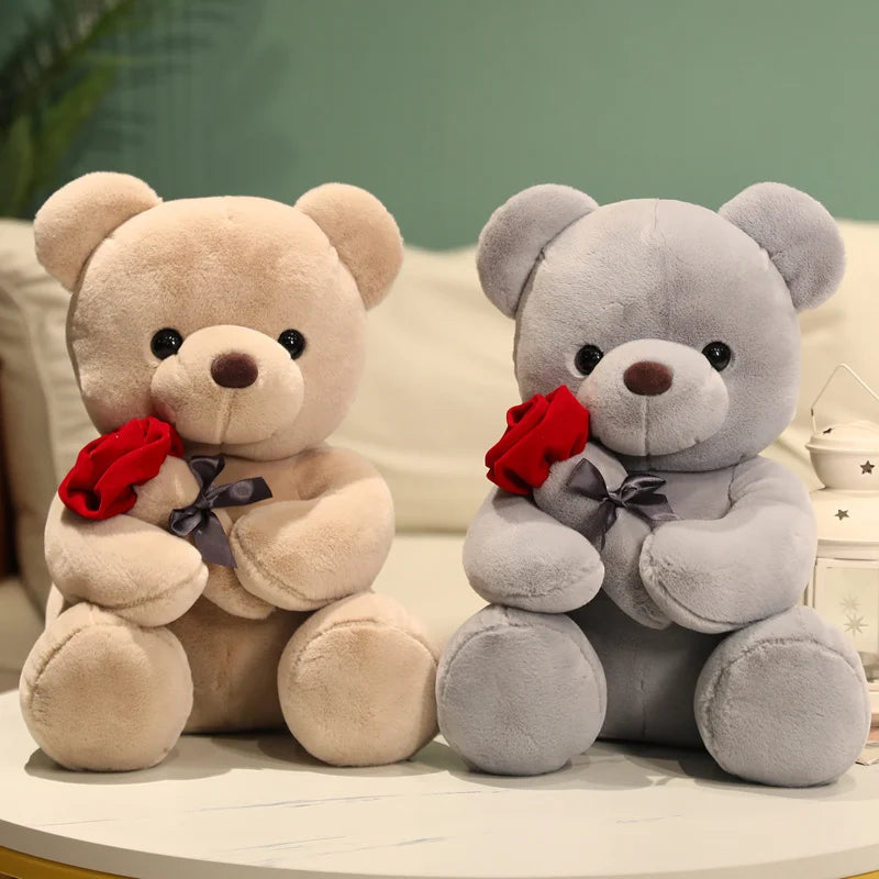 A soft brown teddy bear plush toy holding a red rose, next to a gray teddy bear.