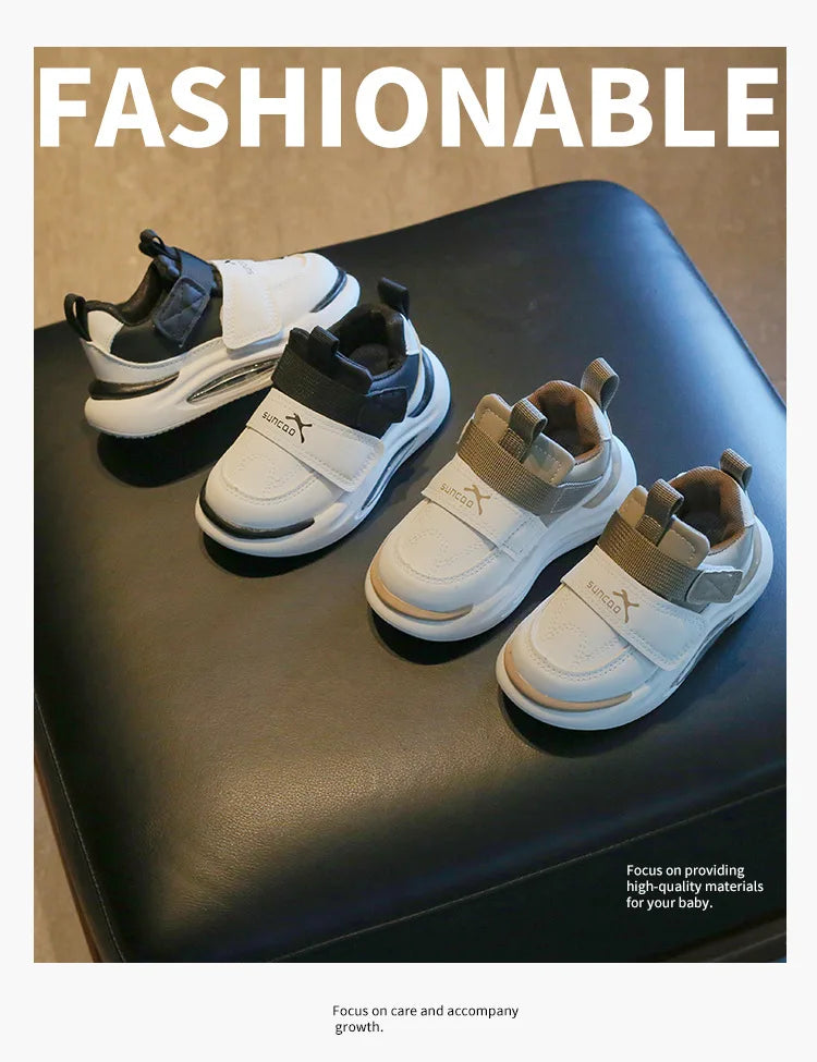 A pair of light gray and white kids' everyday sneakers with easy velcro straps resting on a dark surface.