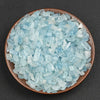 A pile of light blue to translucent aquamarine chips in a shallow brown dish.