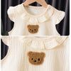 A cream-colored cotton muslin baby romper and hat set featuring a brown bear appliqué.