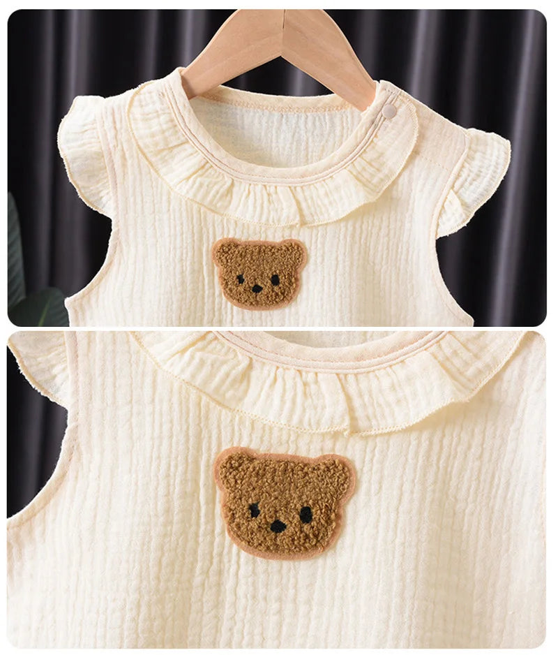 A cream-colored cotton muslin baby romper and hat set featuring a brown bear appliqué.