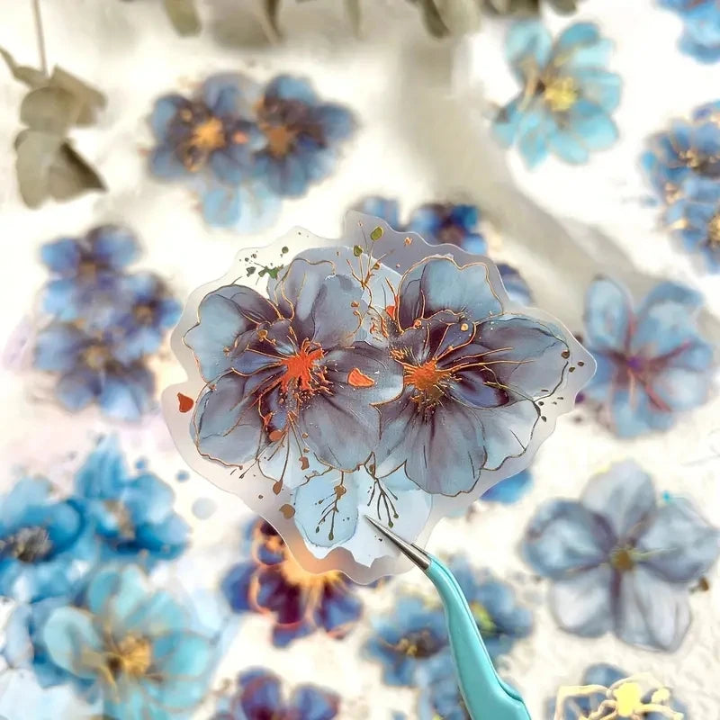 A collection of blue and purple floral hot stamp stickers scattered on a white background.