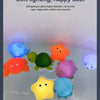 A collection of colorful, soft LED light-up bath toys floating in clear water.