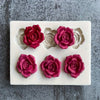 A silicone mold with five pressed rose flower shapes in deep magenta and gray colors.