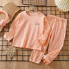 A peach colored long sleeve cotton pajama set for a child, laid out on a wooden grid.