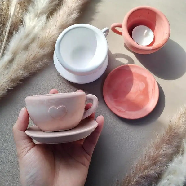 A hand holds a pink heart-shaped silicone mug and a matching pink bowl on a neutral surface.