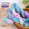 A skein of hand-dyed yarn featuring a vibrant pink and turquoise gradient color is displayed in a woven basket.