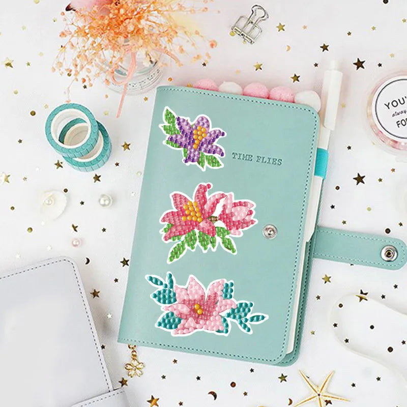 A teal notebook featuring floral designs and stickers, surrounded by glitter and star confetti.