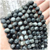 A hand holds a strand of dark gray and black natural stone beads for DIY jewelry making