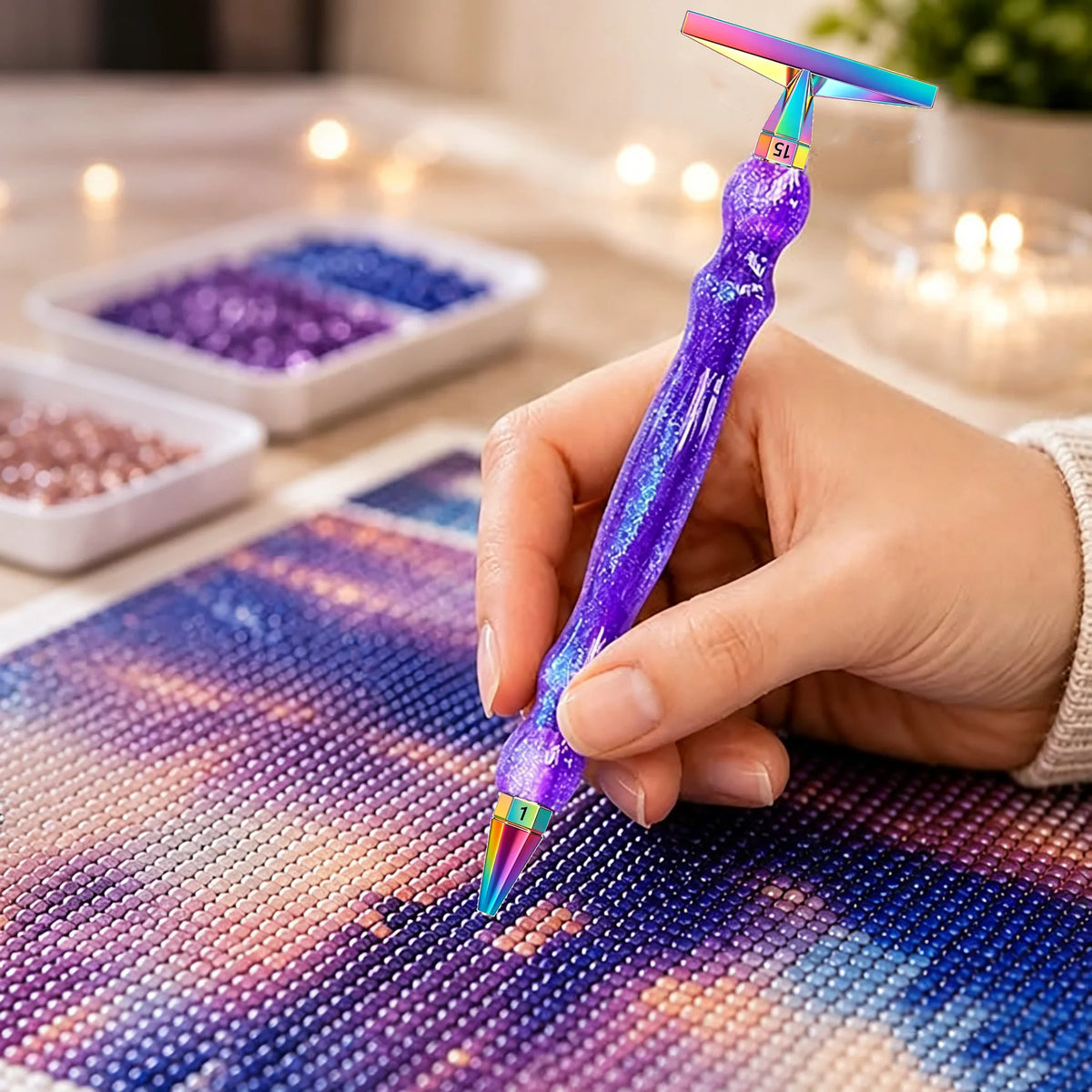 A hand holds a purple diamond painting pen with an interchangeable resin tip, writing on a colorful canvas.