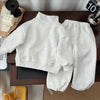 A light gray kids' 2-piece set consisting of a long-sleeve sweater and matching sweatpants laid out on a wooden surface.