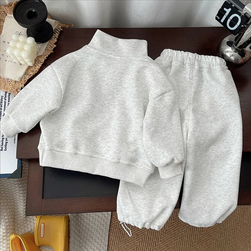 A light gray kids' 2-piece set consisting of a long-sleeve sweater and matching sweatpants laid out on a wooden surface.