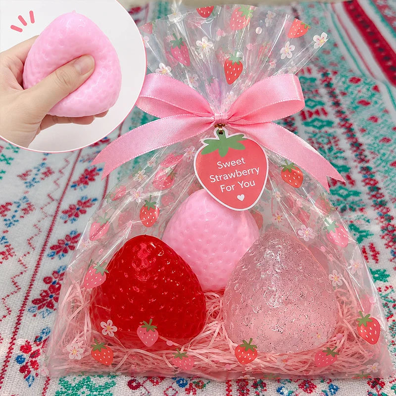 A clear bag filled with pink and red strawberry squishy toys, including a large pink strawberry and a smaller red strawberry.
