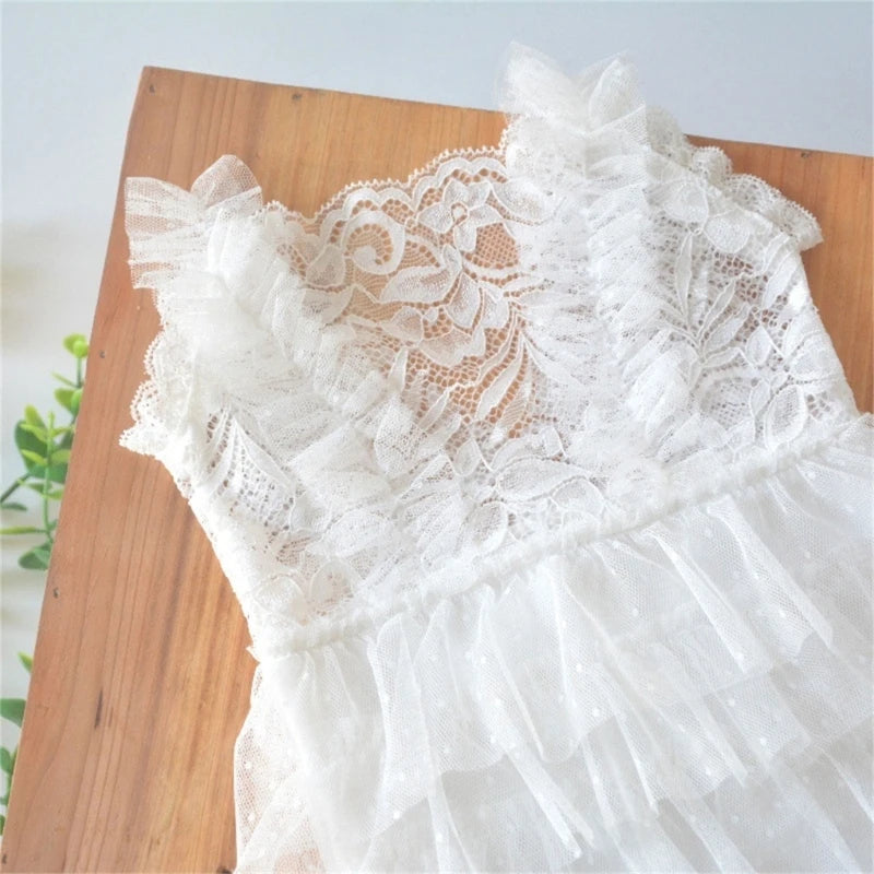 White lace baby romper with delicate floral pattern displayed on a wooden surface.