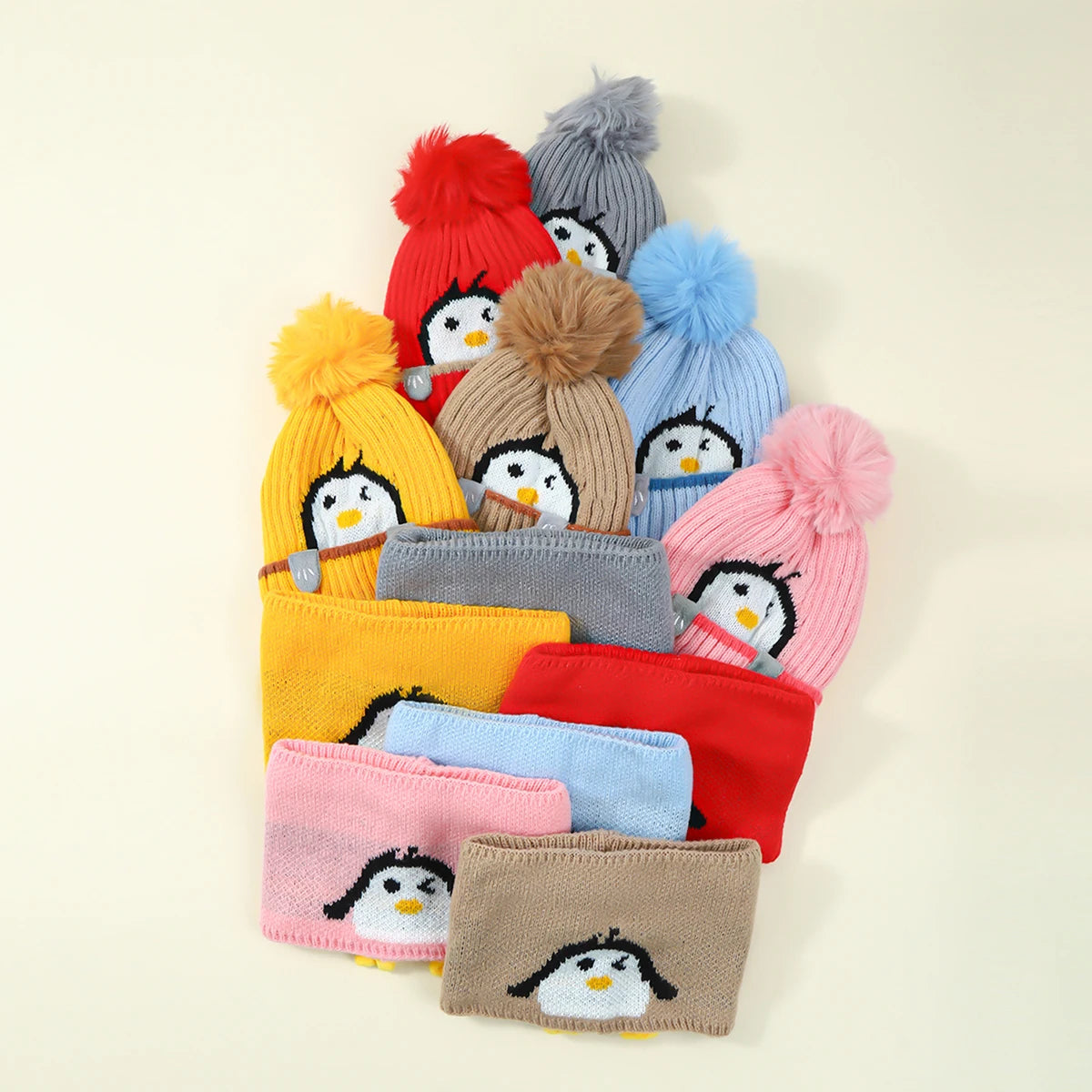 A collection of colorful knit penguin hats and scarves in shades of yellow, gray, blue, and pink.