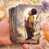 A hand holds a tarot card depicting a woman with curly hair standing by water under a large moon, labeled Three of Wands.