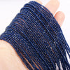 A hand holds a strand of dark blue faceted natural stone beads for DIY jewelry making.