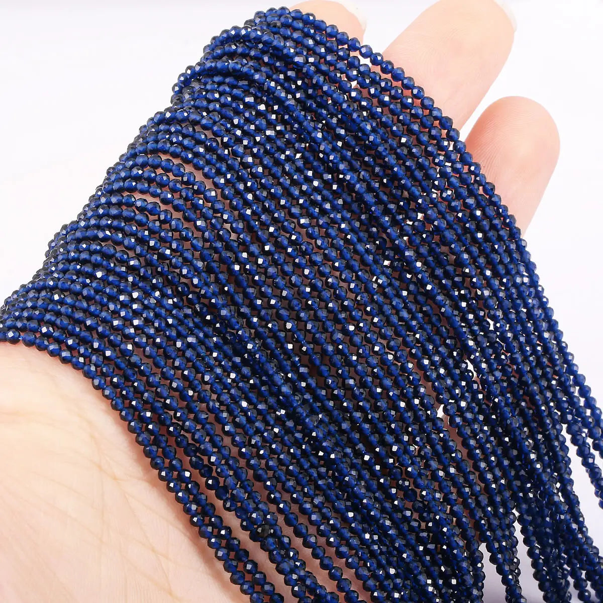 A hand holds a strand of dark blue faceted natural stone beads for DIY jewelry making.