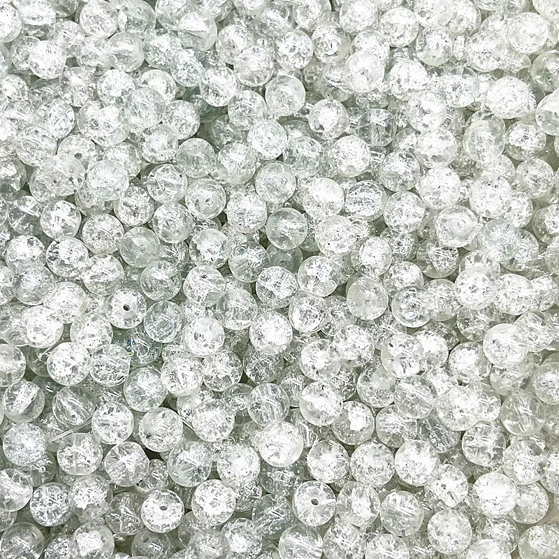 A close-up view of clear round glass crackle beads for jewelry making scattered in a pile.
