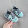 A pair of light mint green and gray breathable mesh toddler walking shoes are being held by a hand.