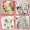 A collection of vintage embroidery stickers is shown on a page of a journal, alongside a glass bottle with similar decorative