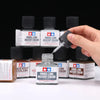 A hand is applying Panel Line Accent Color paint to a bottle of Panel Line Accent Color paint.