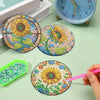 A hand paints a floral diamond painting coaster on a circular piece of fabric, surrounded by other finished coasters and a cl